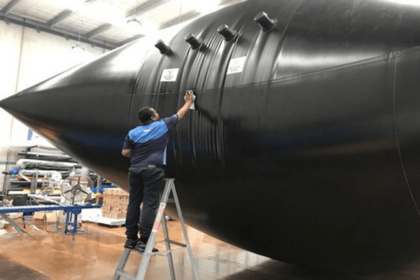 A worker inspecting seams of pressurised liquid fertiliser storage flexitank bladder during factory testing