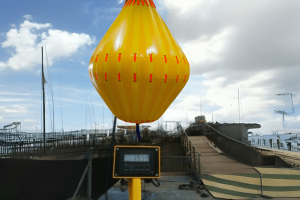 Fleximake water weight bag used for load testing, showing single-point lift setup with digital scale, performing a structural performance test in an onshore environment.